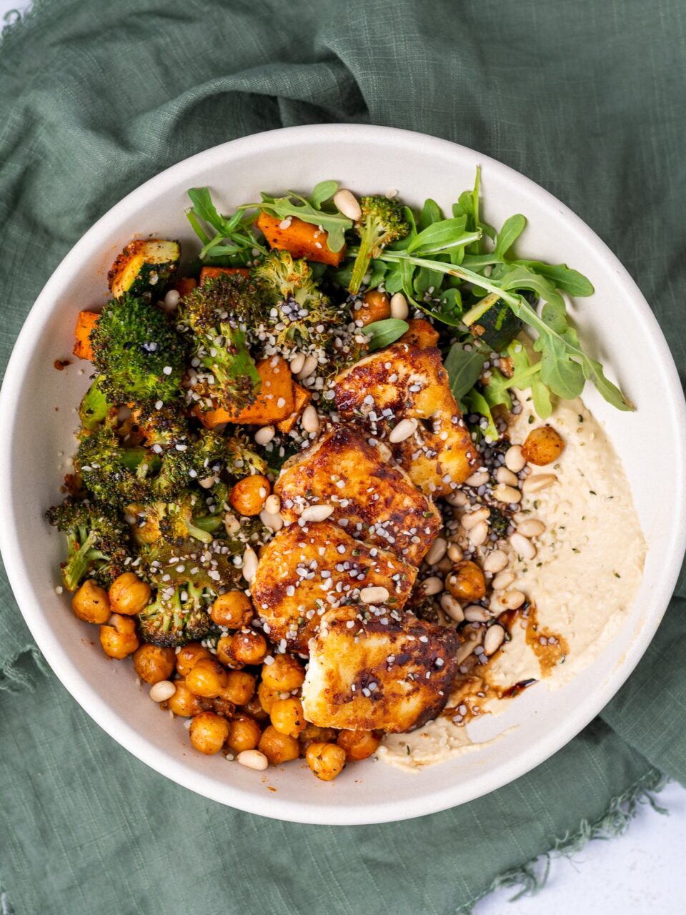 Close-up of a roasted chickpea hummus bowl with a spoon dipping into creamy hummus, showing golden crispy chickpeas, fresh herbs, and a drizzle of golden olive oil