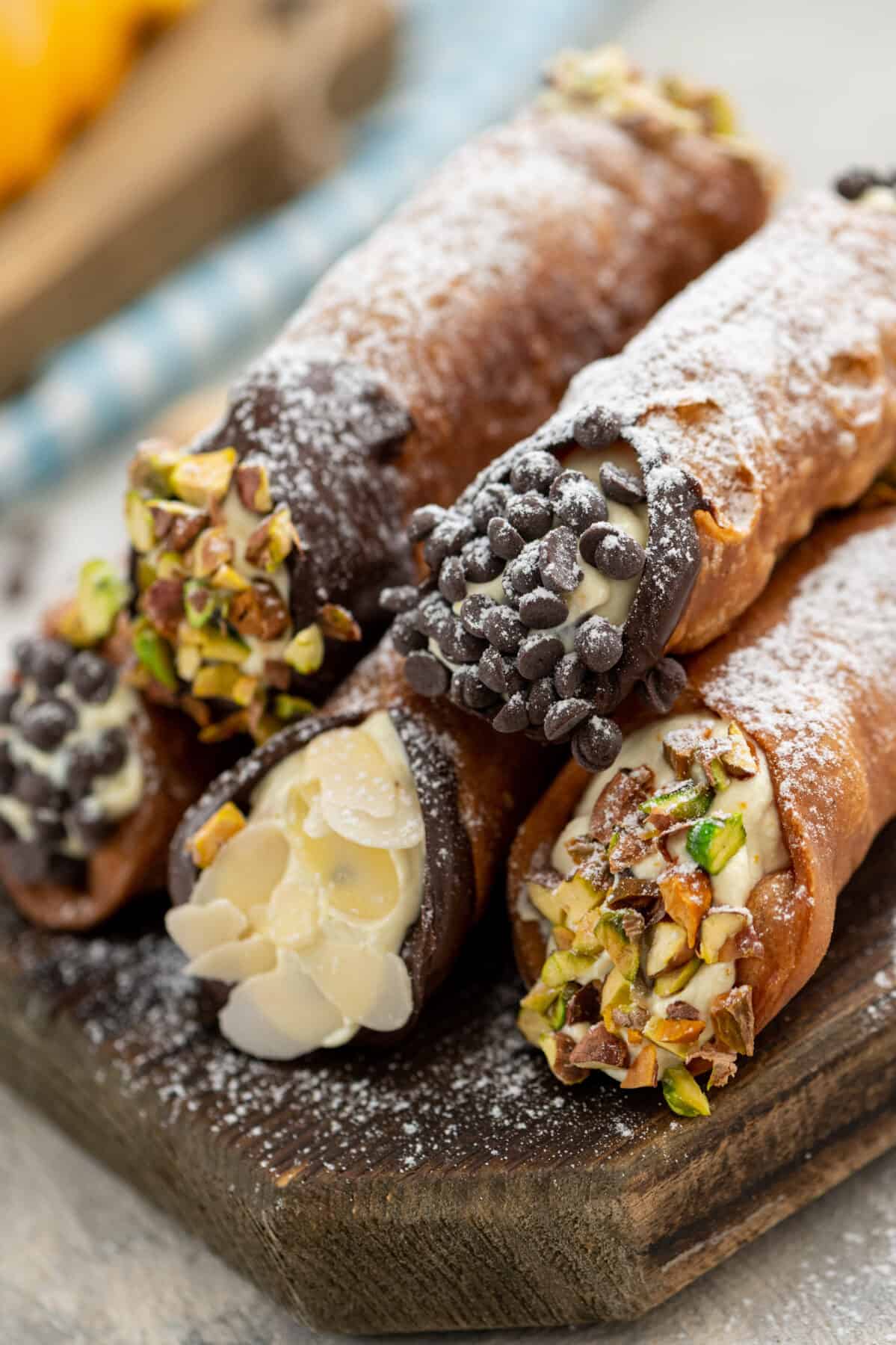 Golden crispy cannoli shells filled with creamy white ricotta mixture, dusted with powdered sugar and garnished with chopped pistachios, arranged on a rustic wooden serving platter