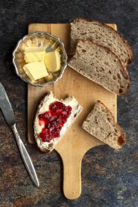 rustic sourdough bread loaf sliced on wooden cutting board with butter and jam nearby