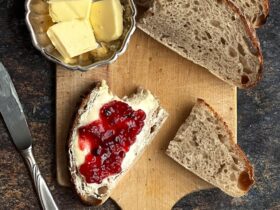 rustic sourdough bread loaf sliced on wooden cutting board with butter and jam nearby