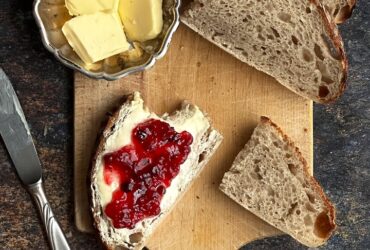 rustic sourdough bread loaf sliced on wooden cutting board with butter and jam nearby