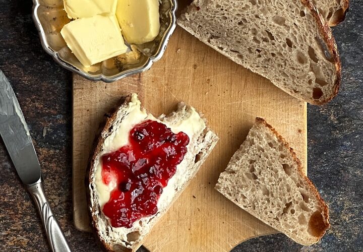 rustic sourdough bread loaf sliced on wooden cutting board with butter and jam nearby