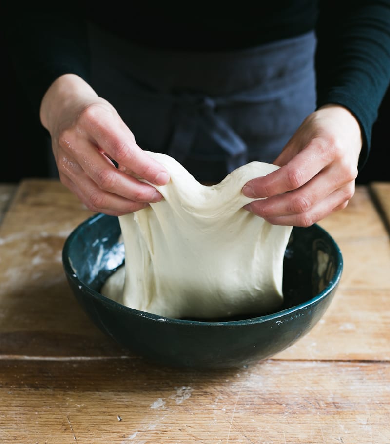 hands performing stretch and fold technique on sourdough dough in large mixing bowl