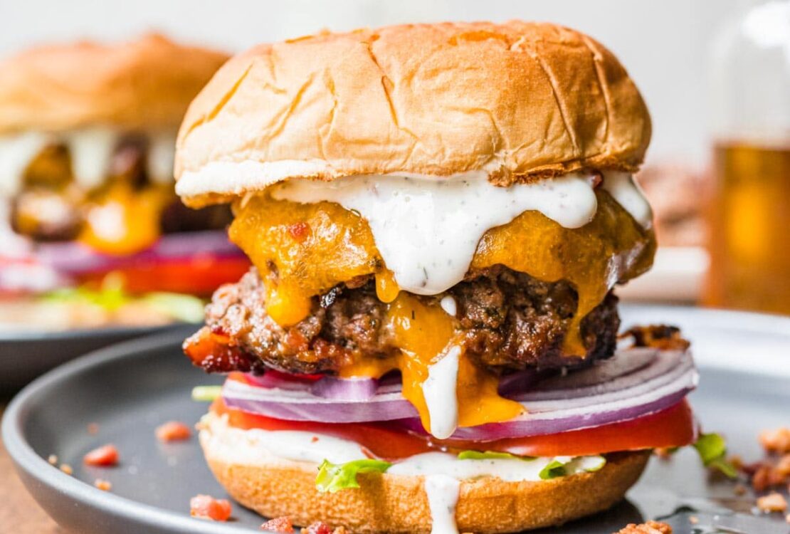 Bacon Ranch Burgers stacked high with crispy bacon, melted cheddar, and ranch drizzle on a wooden board