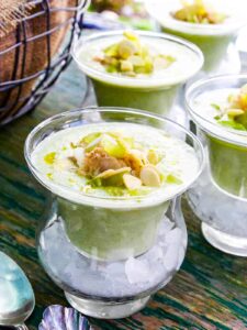 A bowl of vibrant red chilled gazpacho garnished with diced cucumber, croutons, a drizzle of olive oil, and fresh basil on a rustic wooden table