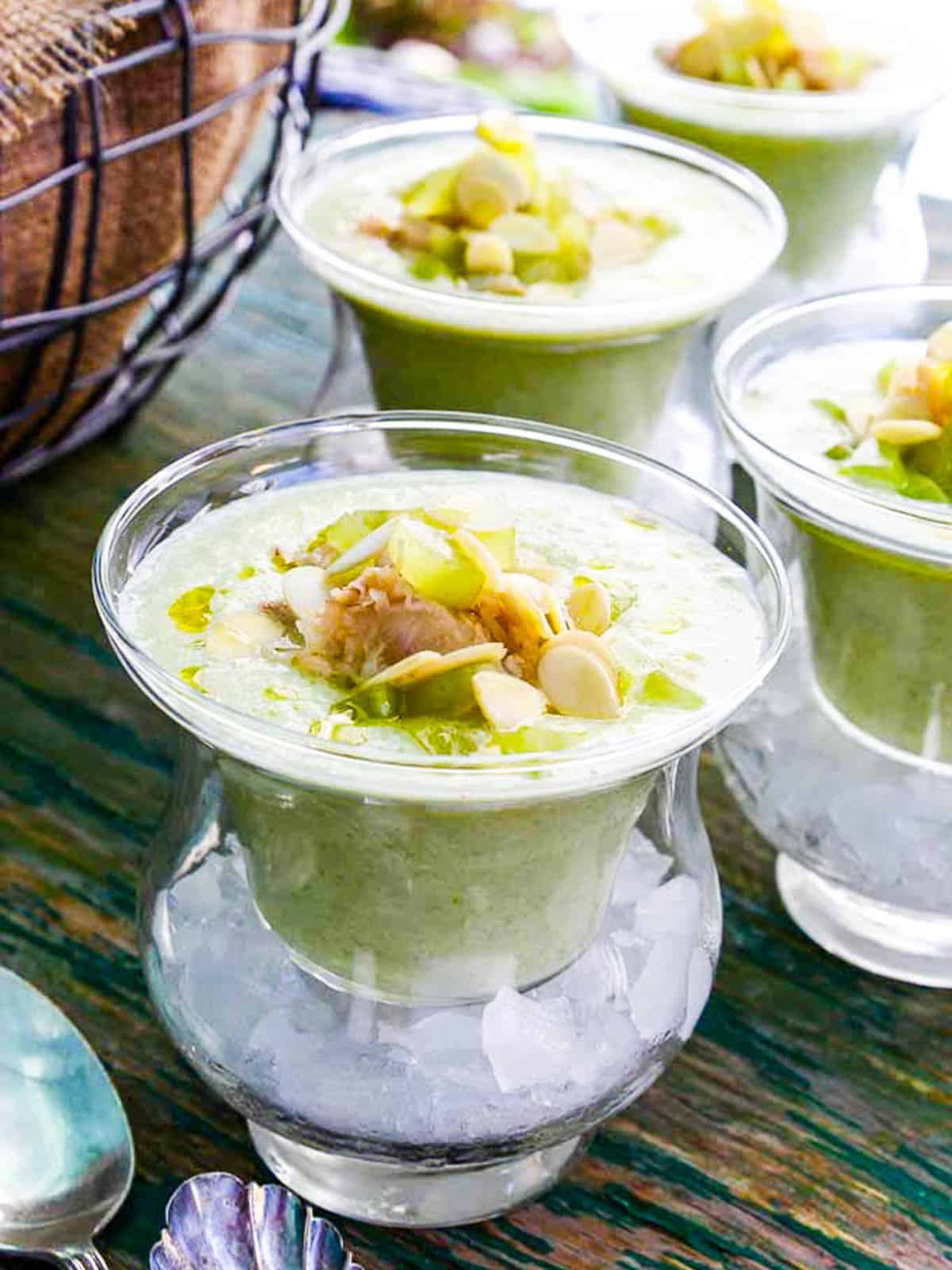 A bowl of vibrant red chilled gazpacho garnished with diced cucumber, croutons, a drizzle of olive oil, and fresh basil on a rustic wooden table