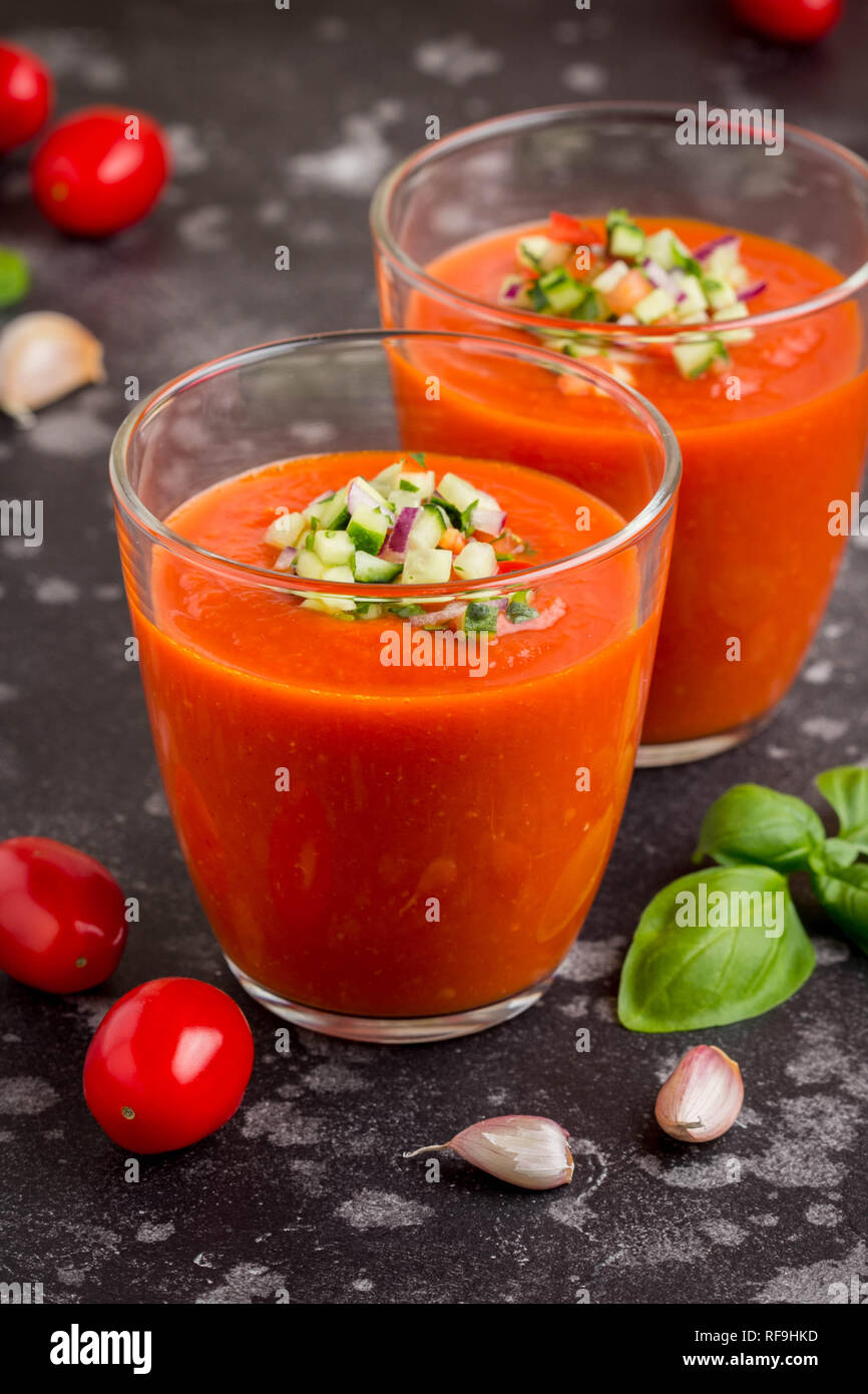 Close-up of a glass of chilled gazpacho with a garnish of finely diced vegetables, a drizzle of olive oil, and a basil leaf, served alongside crusty bread on a linen napkin