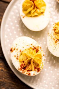 Classic deviled eggs on a white serving platter dusted with paprika and garnished with fresh chives, shot overhead on a rustic wooden picnic table