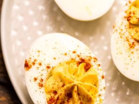Classic deviled eggs on a white serving platter dusted with paprika and garnished with fresh chives, shot overhead on a rustic wooden picnic table