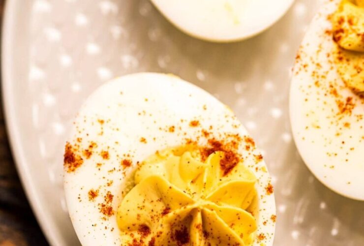 Classic deviled eggs on a white serving platter dusted with paprika and garnished with fresh chives, shot overhead on a rustic wooden picnic table