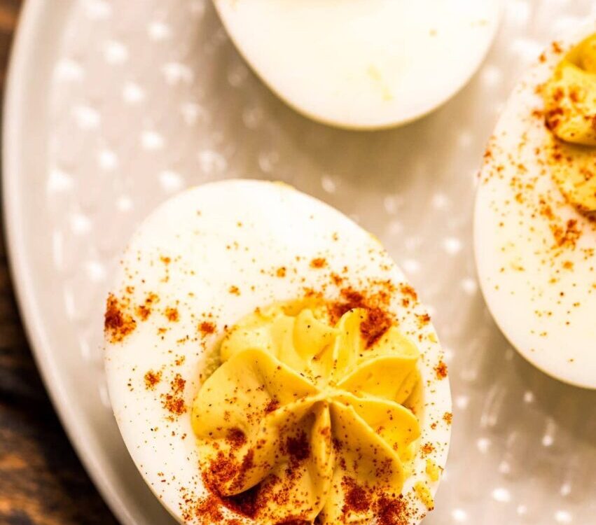 Classic deviled eggs on a white serving platter dusted with paprika and garnished with fresh chives, shot overhead on a rustic wooden picnic table