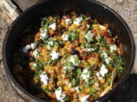 Dutch Oven Campfire Nachos loaded with melted cheese, black beans, salsa, and toppings served straight from a cast iron Dutch oven at a campfire