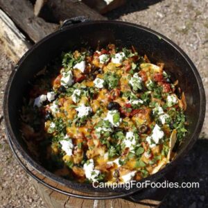 Dutch Oven Campfire Nachos loaded with melted cheese, black beans, salsa, and toppings served straight from a cast iron Dutch oven at a campfire