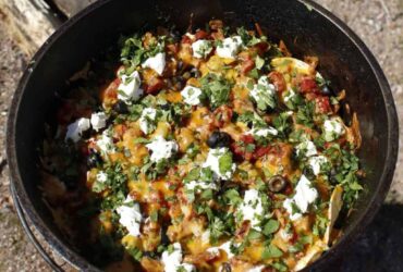 Dutch Oven Campfire Nachos loaded with melted cheese, black beans, salsa, and toppings served straight from a cast iron Dutch oven at a campfire