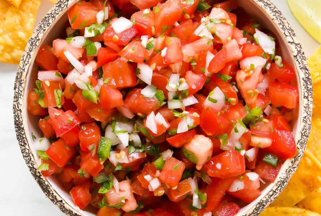Fresh Pico de Gallo in a rustic bowl with tortilla chips, diced tomatoes, cilantro, and lime wedges on a wooden board