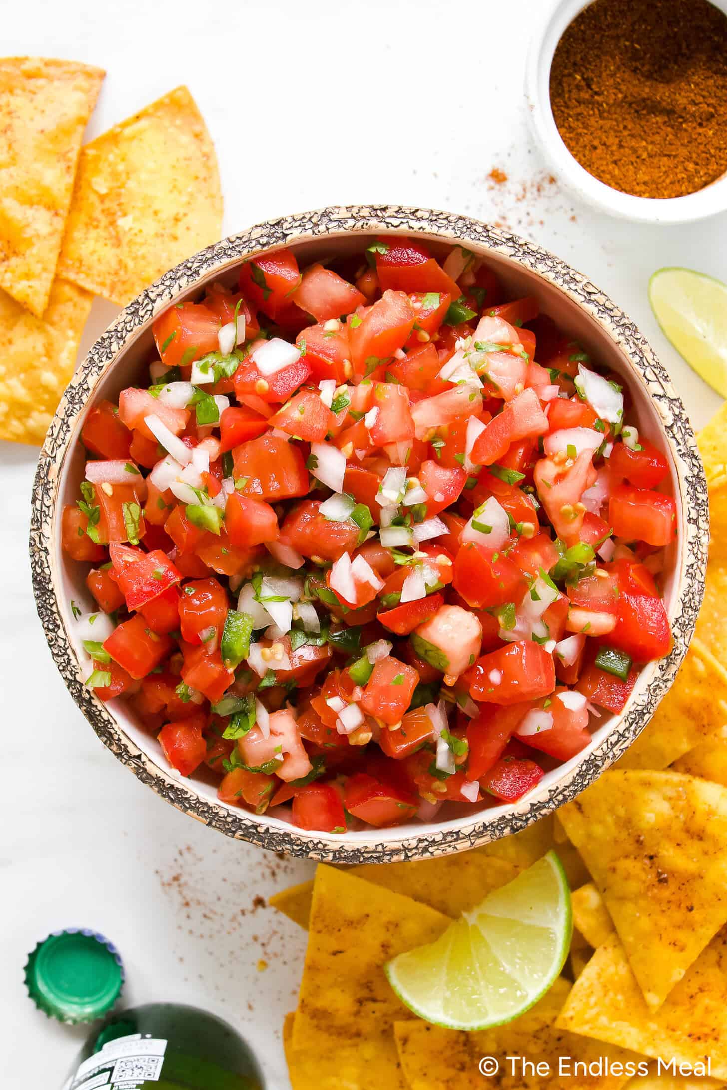 Fresh Pico de Gallo in a rustic bowl with tortilla chips, diced tomatoes, cilantro, and lime wedges on a wooden board