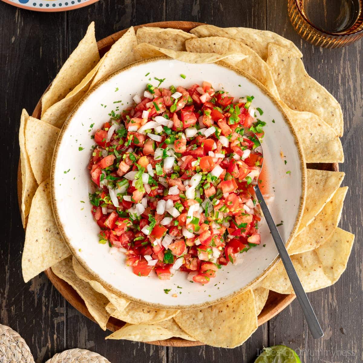Overhead flat lay of fresh pico de gallo ingredients: diced roma tomatoes, white onion, jalapeño, cilantro, lime, and salt on a marble surface