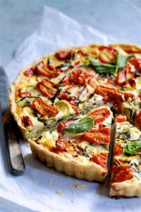 Grilled vegetable and goat cheese tart sliced on a rustic wooden board with fresh herbs and a golden flaky whole wheat crust
