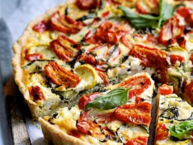 Grilled vegetable and goat cheese tart sliced on a rustic wooden board with fresh herbs and a golden flaky whole wheat crust