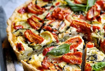 Grilled vegetable and goat cheese tart sliced on a rustic wooden board with fresh herbs and a golden flaky whole wheat crust