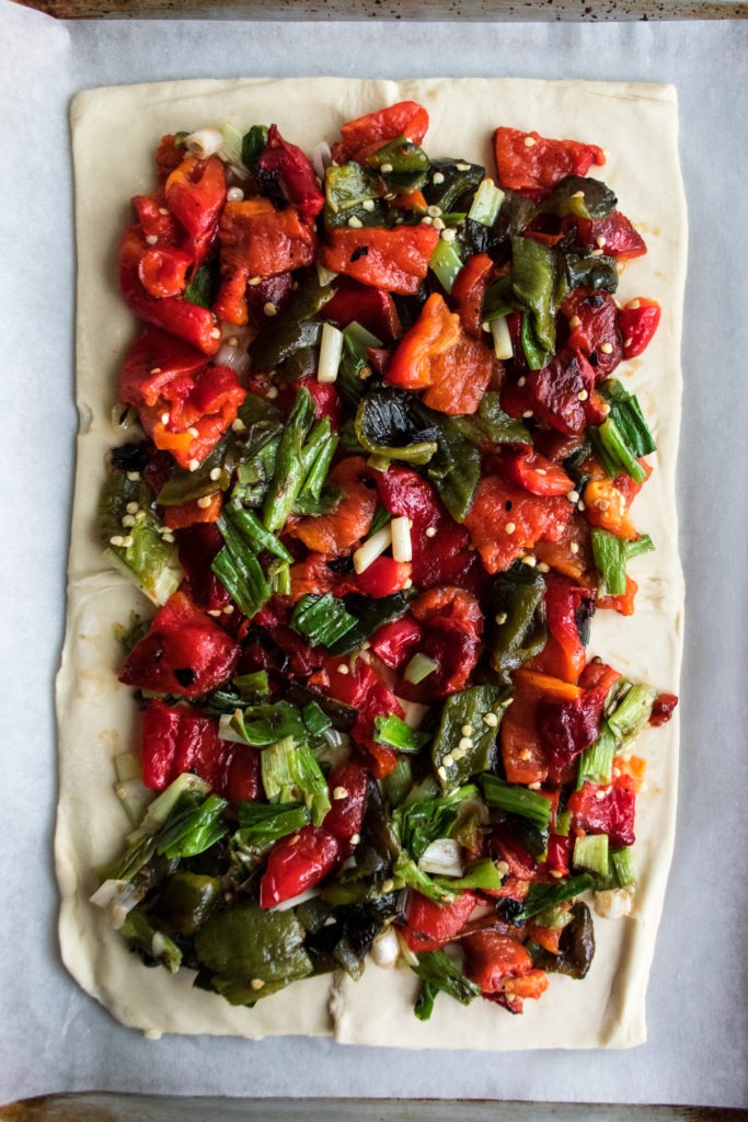 Grilled zucchini, red bell pepper, and red onion slices arranged on a grill pan beside a bowl of herbed goat cheese mixture and a rolled whole wheat tart crust