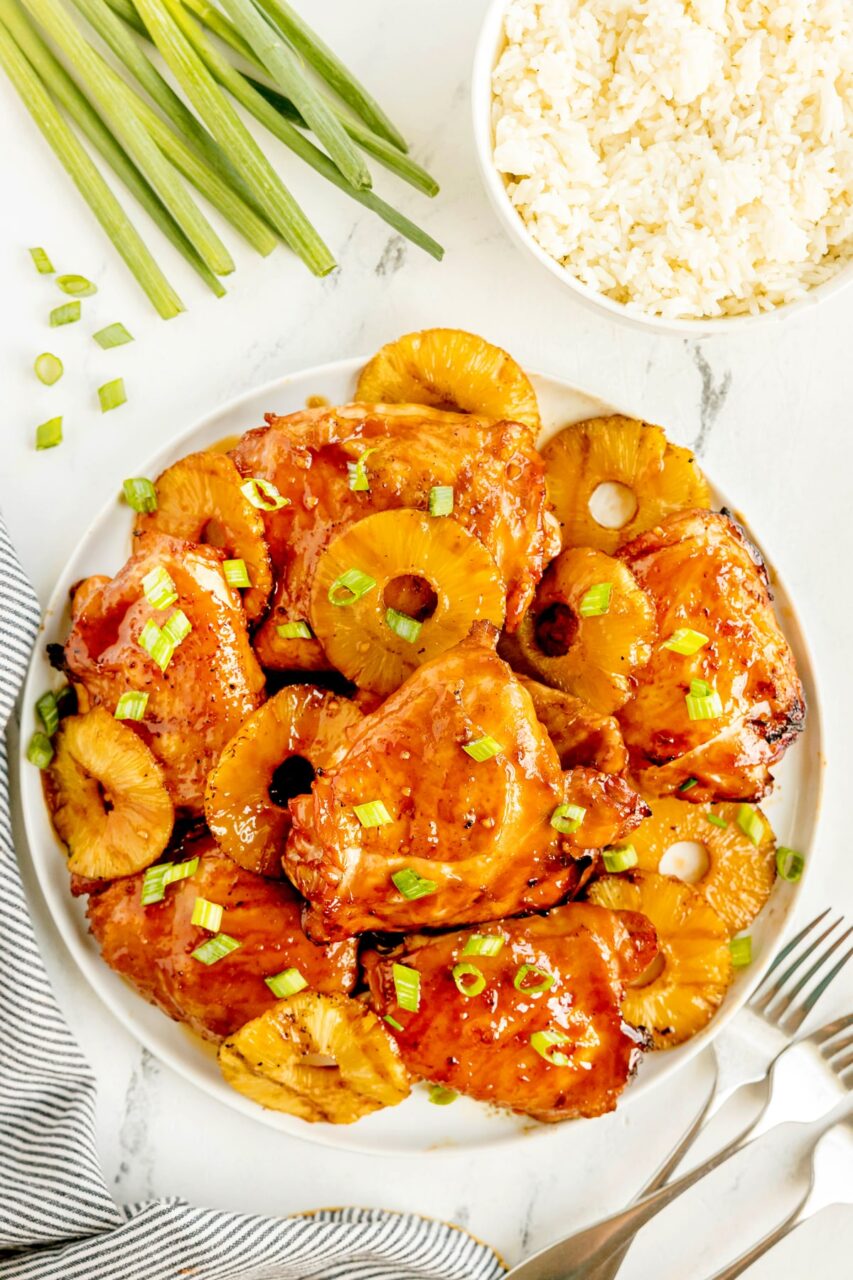 Huli Huli Chicken plated on a wooden board with caramelized pineapple glaze and fresh green onions garnish