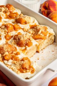golden peach cobbler in a white baking dish with bubbling peach filling and fluffy biscuit topping dusted with cinnamon sugar