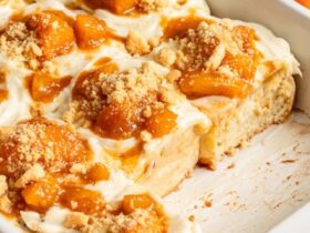 golden peach cobbler in a white baking dish with bubbling peach filling and fluffy biscuit topping dusted with cinnamon sugar