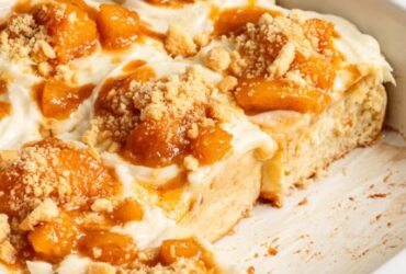 golden peach cobbler in a white baking dish with bubbling peach filling and fluffy biscuit topping dusted with cinnamon sugar