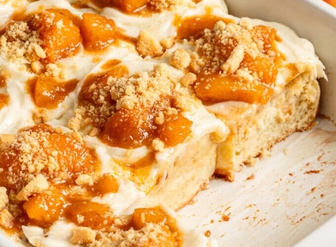 golden peach cobbler in a white baking dish with bubbling peach filling and fluffy biscuit topping dusted with cinnamon sugar