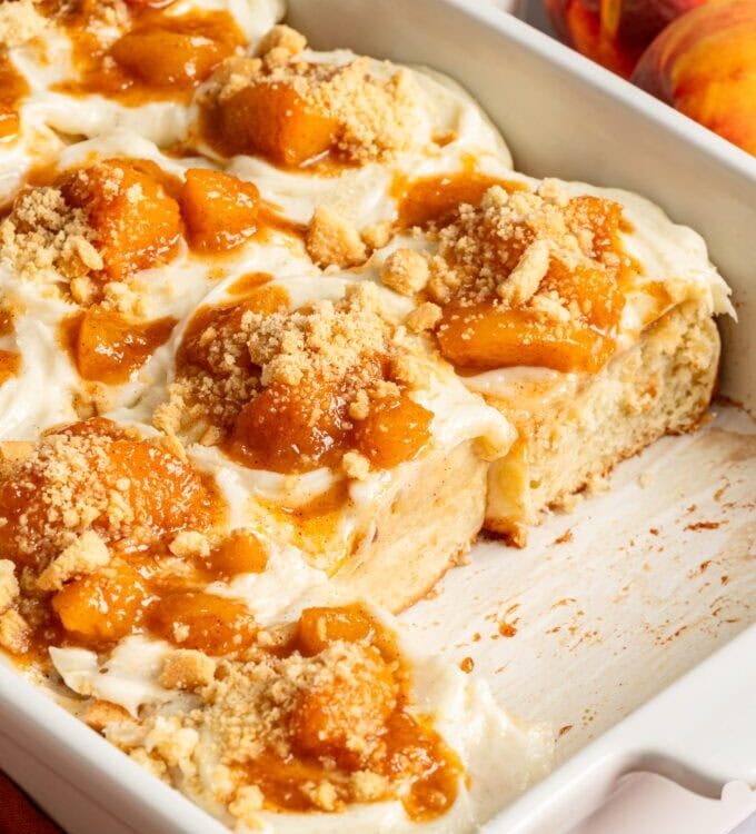 golden peach cobbler in a white baking dish with bubbling peach filling and fluffy biscuit topping dusted with cinnamon sugar