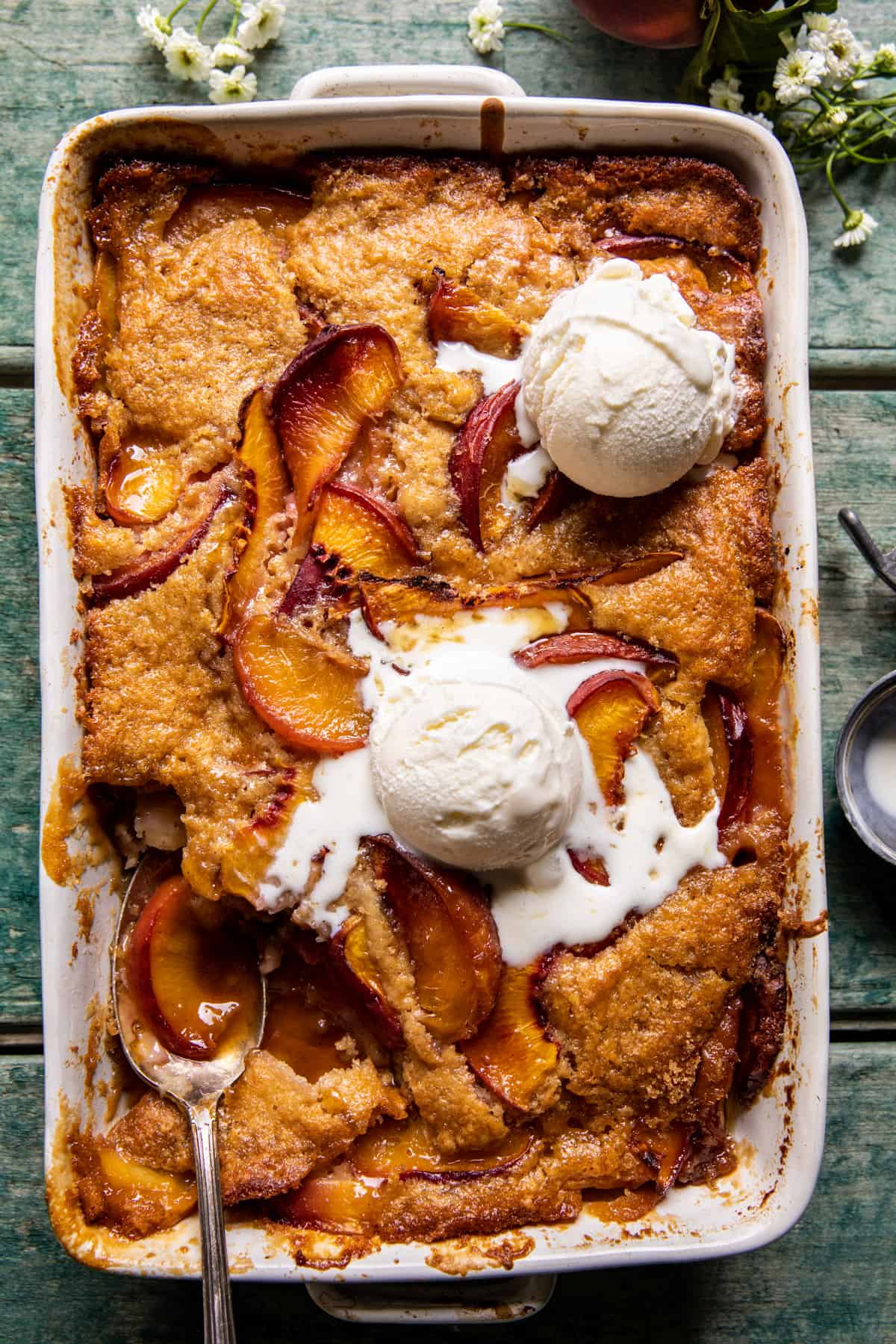 flat lay of peach cobbler ingredients including fresh peaches, flour, butter, buttermilk, cinnamon, and brown sugar on a rustic wooden surface