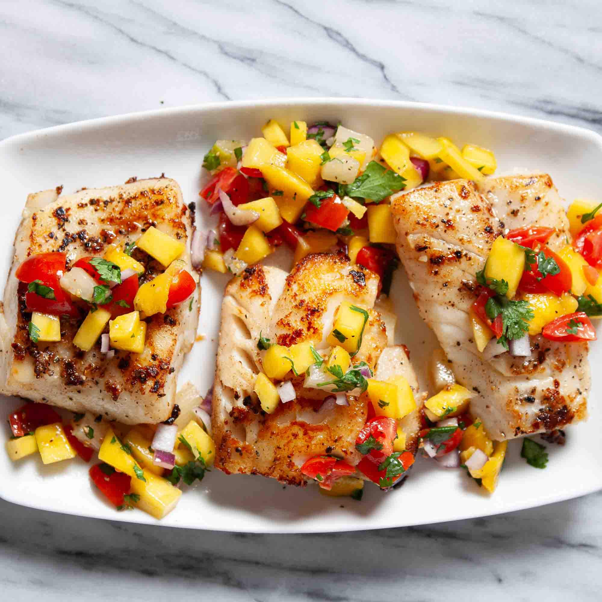 Close-up of peach mango salsa spooned over a piece of seared mahi-mahi on a white plate with lime wedges and cilantro