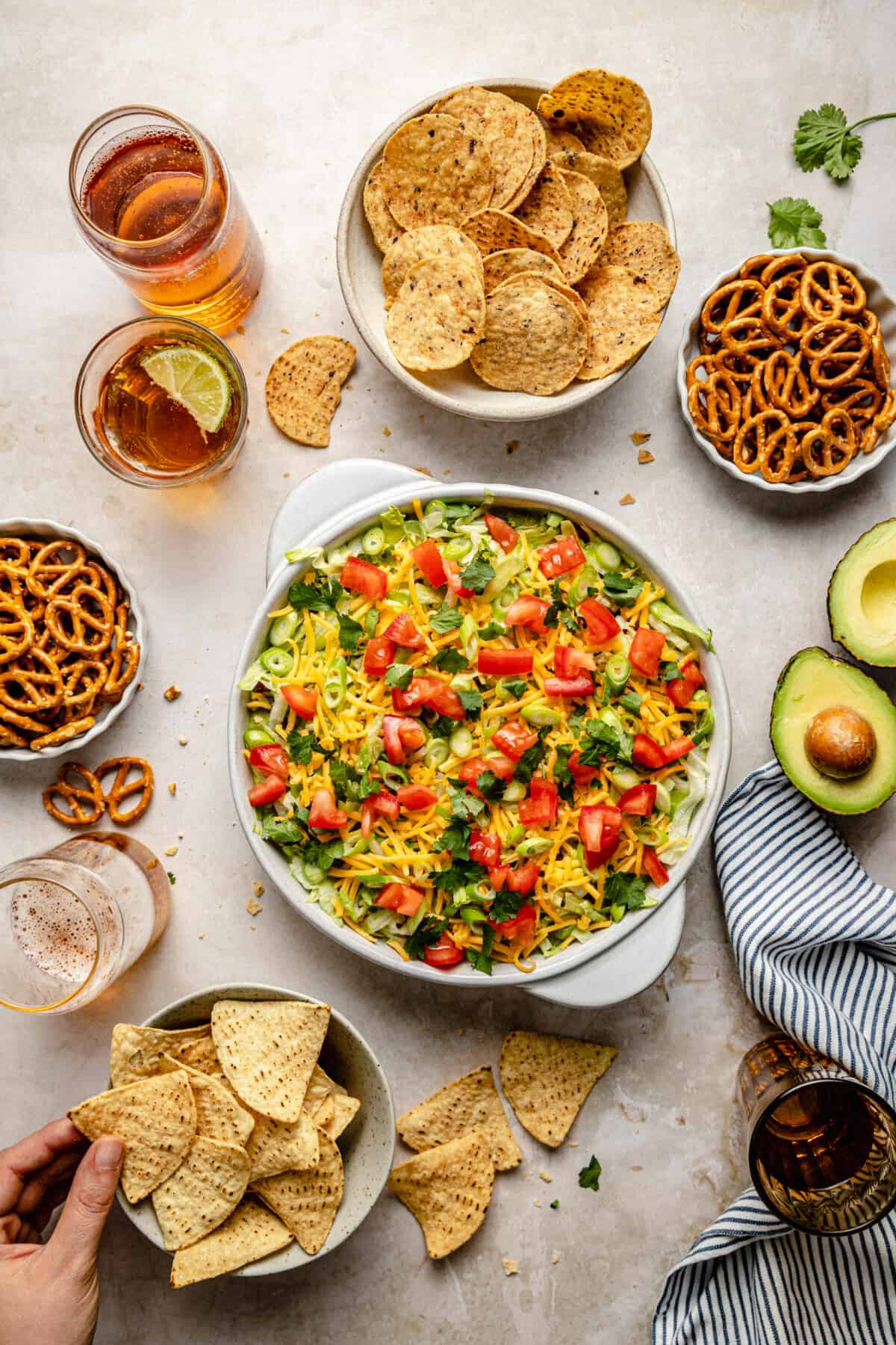 Overhead flat lay of Seven Layer Dip ingredients including refried beans, sour cream, guacamole, salsa, shredded cheese, black olives, tomatoes, and green onions in small prep bowls