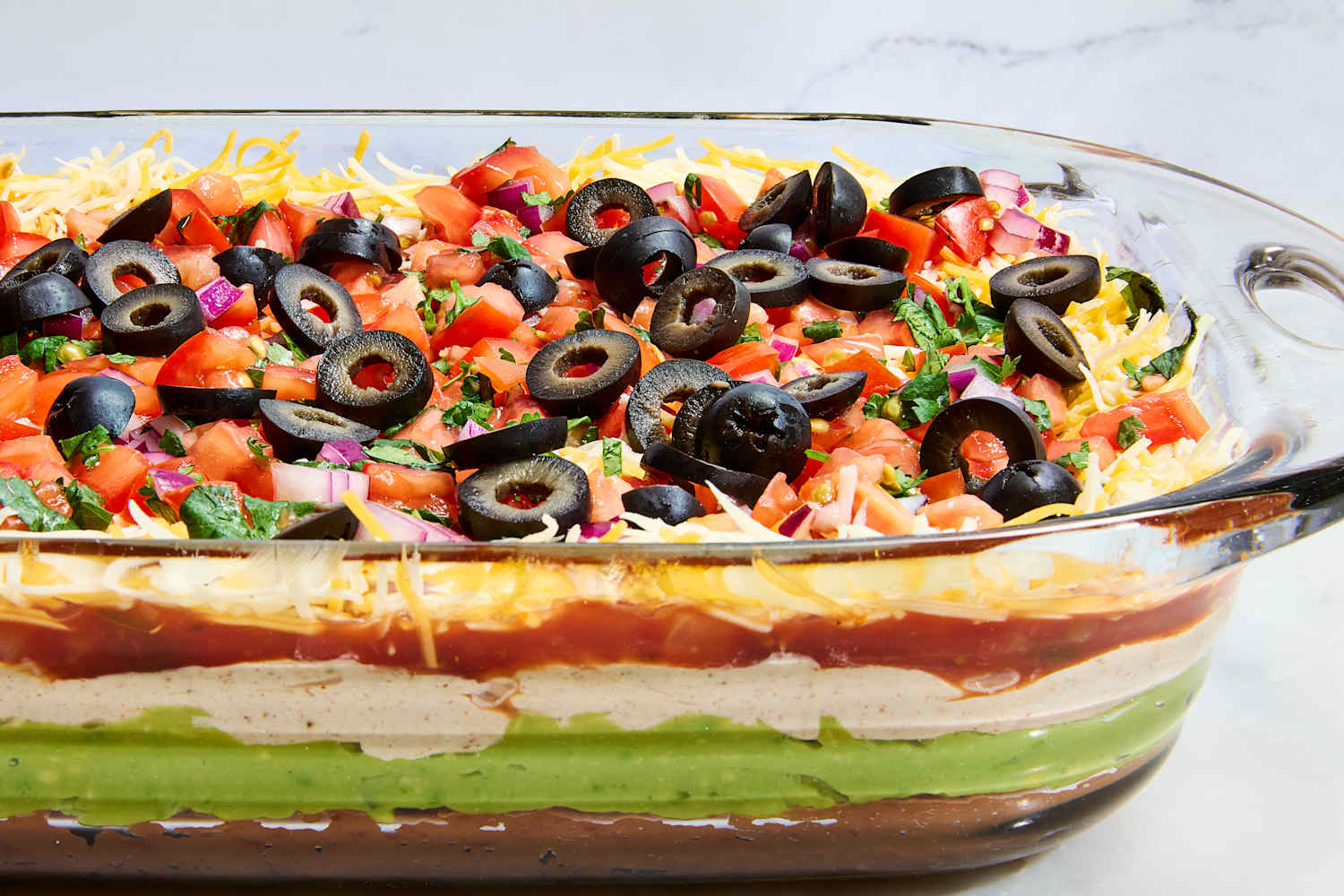 Close-up of a chip scooping through all seven layers of Seven Layer Dip showing the beautiful cross-section of beans, guacamole, sour cream, salsa, cheese, and fresh toppings