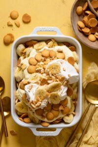 A beautiful overhead shot of classic Southern banana pudding in a large trifle dish, showing golden vanilla wafer layers, sliced bananas, and fluffy whipped topping garnished with crushed wafers