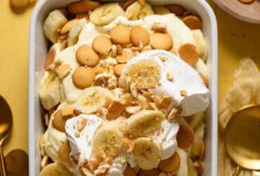 A beautiful overhead shot of classic Southern banana pudding in a large trifle dish, showing golden vanilla wafer layers, sliced bananas, and fluffy whipped topping garnished with crushed wafers