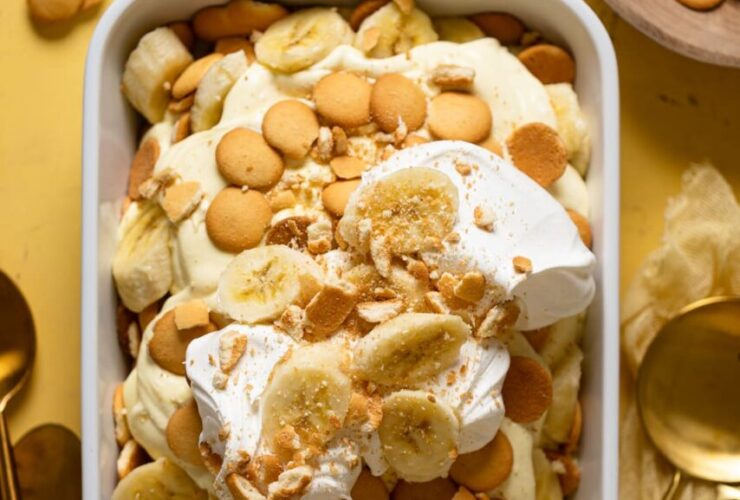 A beautiful overhead shot of classic Southern banana pudding in a large trifle dish, showing golden vanilla wafer layers, sliced bananas, and fluffy whipped topping garnished with crushed wafers