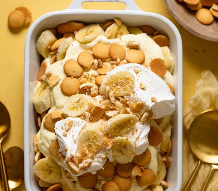 A beautiful overhead shot of classic Southern banana pudding in a large trifle dish, showing golden vanilla wafer layers, sliced bananas, and fluffy whipped topping garnished with crushed wafers