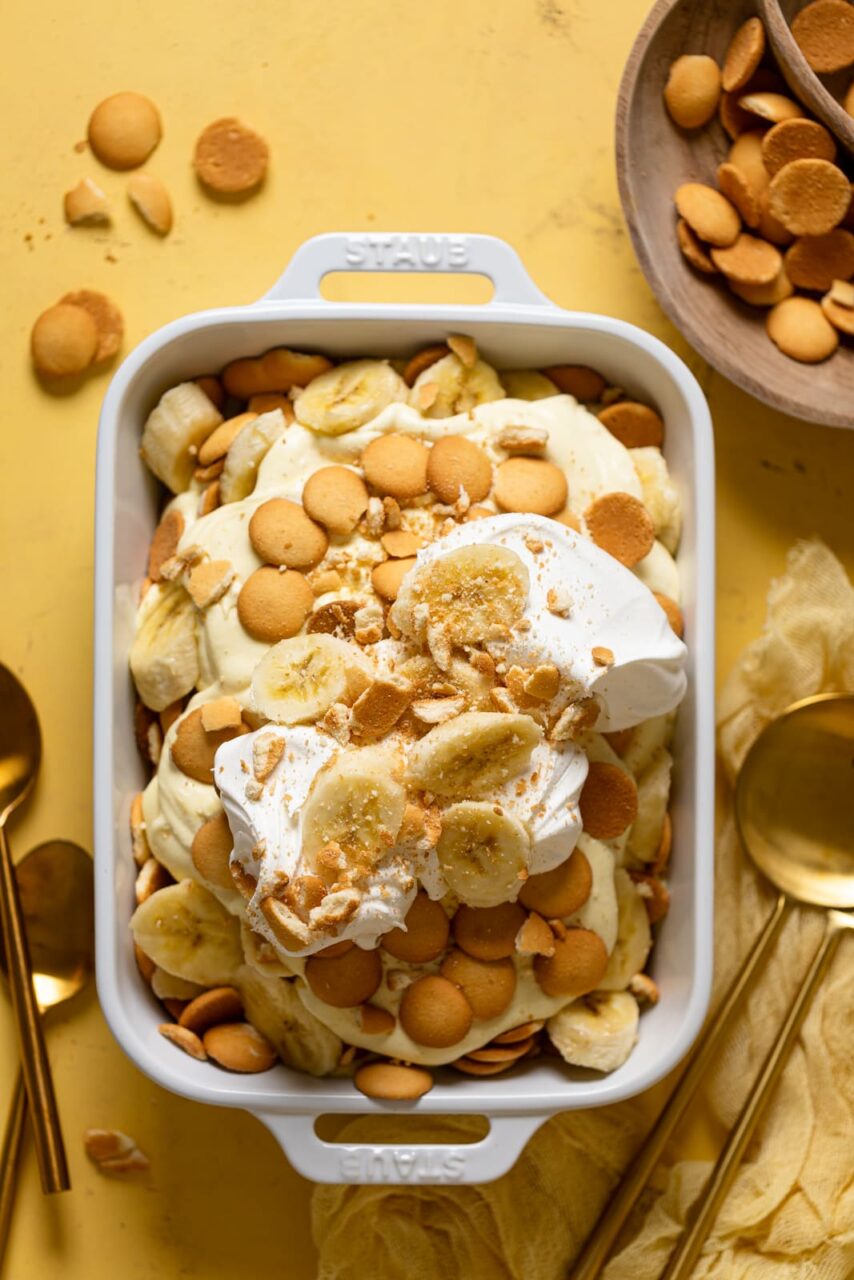 A beautiful overhead shot of classic Southern banana pudding in a large trifle dish, showing golden vanilla wafer layers, sliced bananas, and fluffy whipped topping garnished with crushed wafers