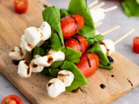 Caprese skewers arranged on a white marble board with balsamic glaze drizzle, fresh basil leaves, and cherry tomatoes