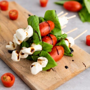 Caprese skewers arranged on a white marble board with balsamic glaze drizzle, fresh basil leaves, and cherry tomatoes