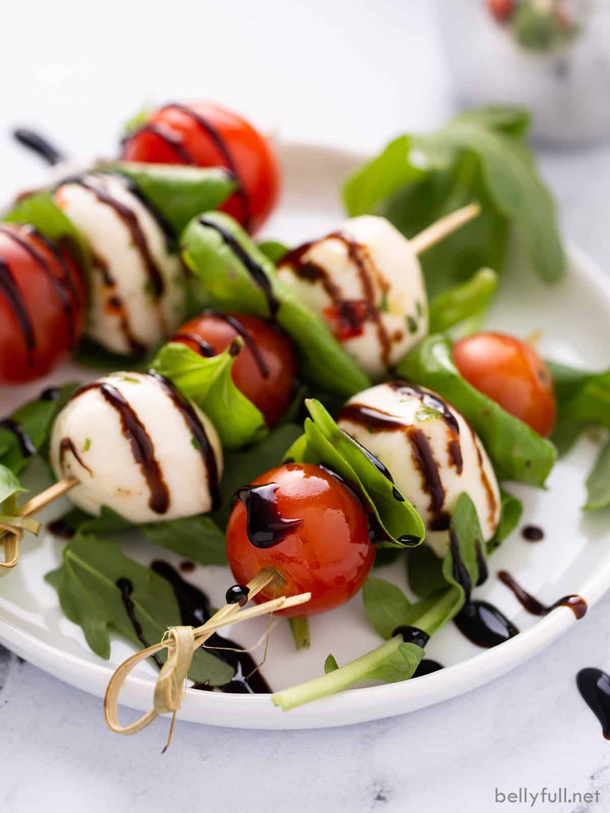 Close-up of a single Caprese skewer held up showing layers of cherry tomato, fresh mozzarella, and basil with balsamic glaze