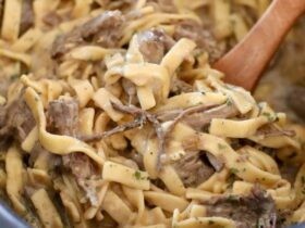 Crockpot beef and noodles served in a wide bowl with tender shredded beef over thick egg noodles coated in rich brown gravy, garnished with fresh parsley