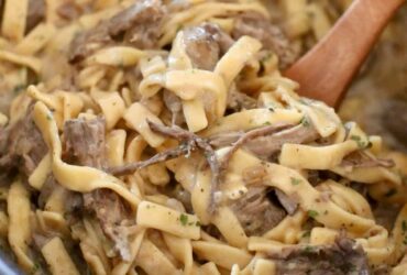Crockpot beef and noodles served in a wide bowl with tender shredded beef over thick egg noodles coated in rich brown gravy, garnished with fresh parsley