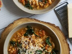 A rustic white bowl filled with Crockpot Pasta e Fagioli — thick tomato broth with ditalini pasta, kidney beans, cannellini beans, and ground beef, garnished with freshly grated Parmesan and chopped fresh parsley, photographed on a wooden farmhouse table with crusty bread on the side