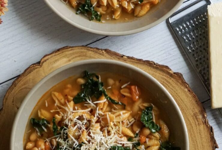 A rustic white bowl filled with Crockpot Pasta e Fagioli — thick tomato broth with ditalini pasta, kidney beans, cannellini beans, and ground beef, garnished with freshly grated Parmesan and chopped fresh parsley, photographed on a wooden farmhouse table with crusty bread on the side