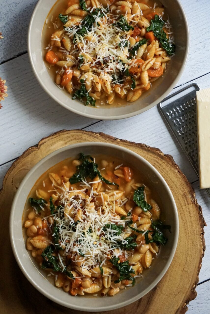 A rustic white bowl filled with Crockpot Pasta e Fagioli — thick tomato broth with ditalini pasta, kidney beans, cannellini beans, and ground beef, garnished with freshly grated Parmesan and chopped fresh parsley, photographed on a wooden farmhouse table with crusty bread on the side