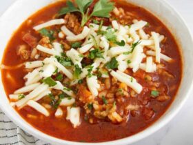 Crockpot Stuffed Pepper Soup served in a white bowl with a spoon, garnished with fresh parsley and shredded cheese on a rustic wooden table