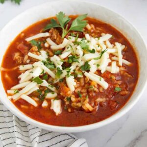 Crockpot Stuffed Pepper Soup served in a white bowl with a spoon, garnished with fresh parsley and shredded cheese on a rustic wooden table